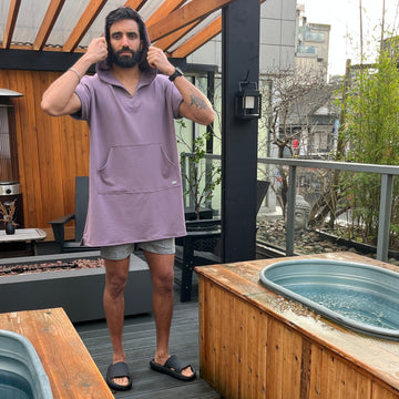 Man wearing a purple shirt and shorts on a wooden deck with cold plunge tubs.