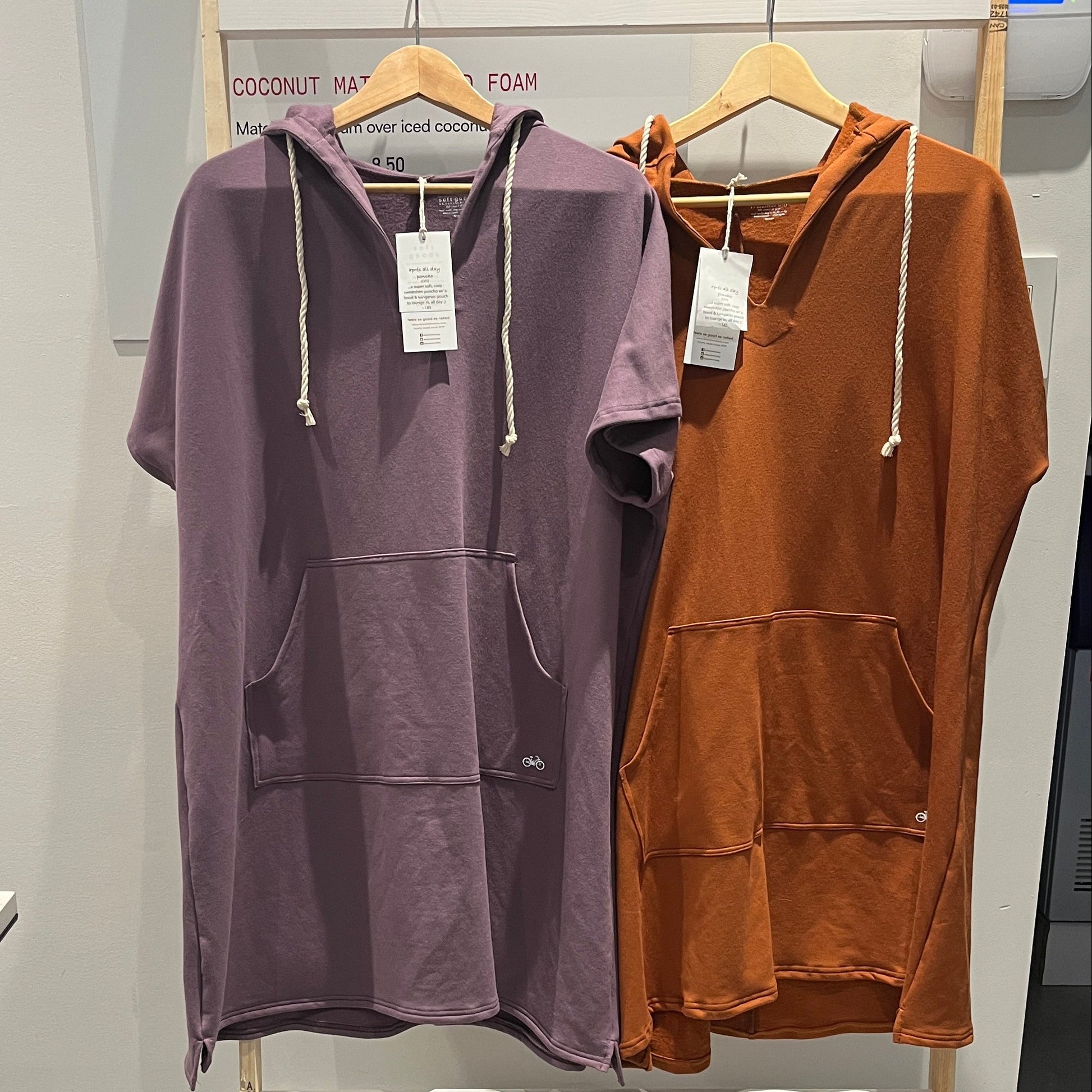 Two hoodies, one purple and one purple, hanging on a rack with tags.