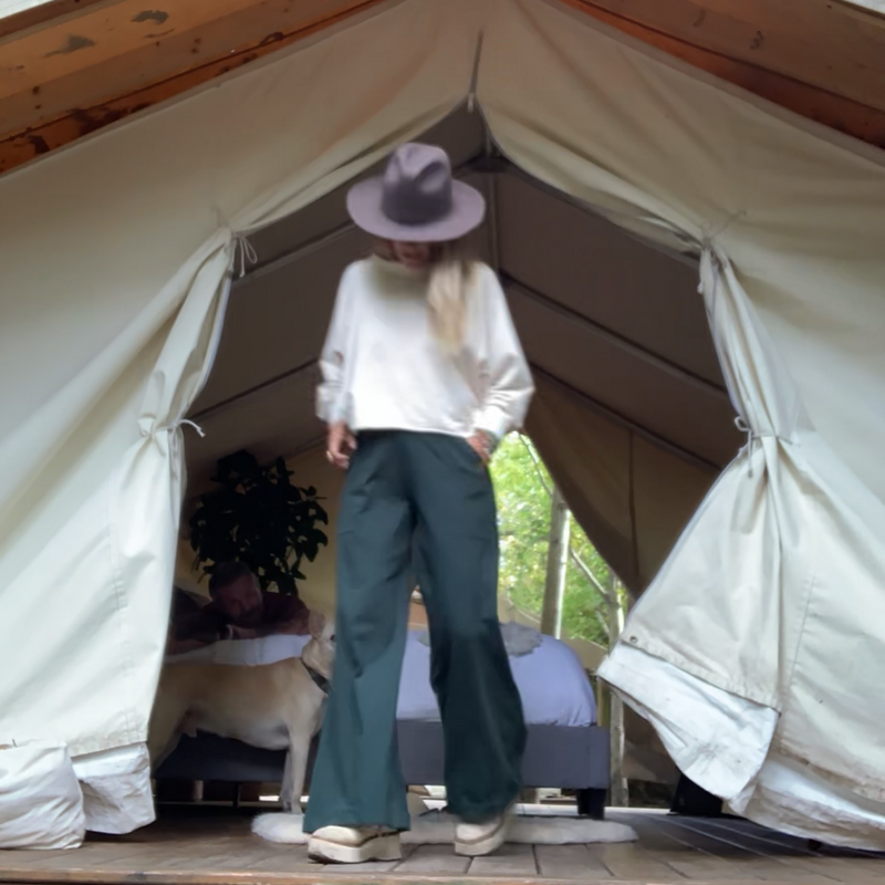 woman in a glamping safari tent wearing a ccream sweatshirt with emerald trouser in the forest 