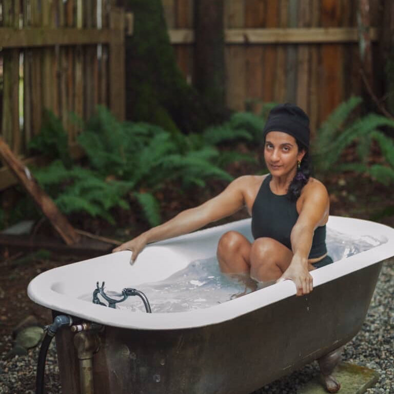 Person sitting in natural fiber sauna suit in an outdoor bathtub with a wooden fence and greenery in the background