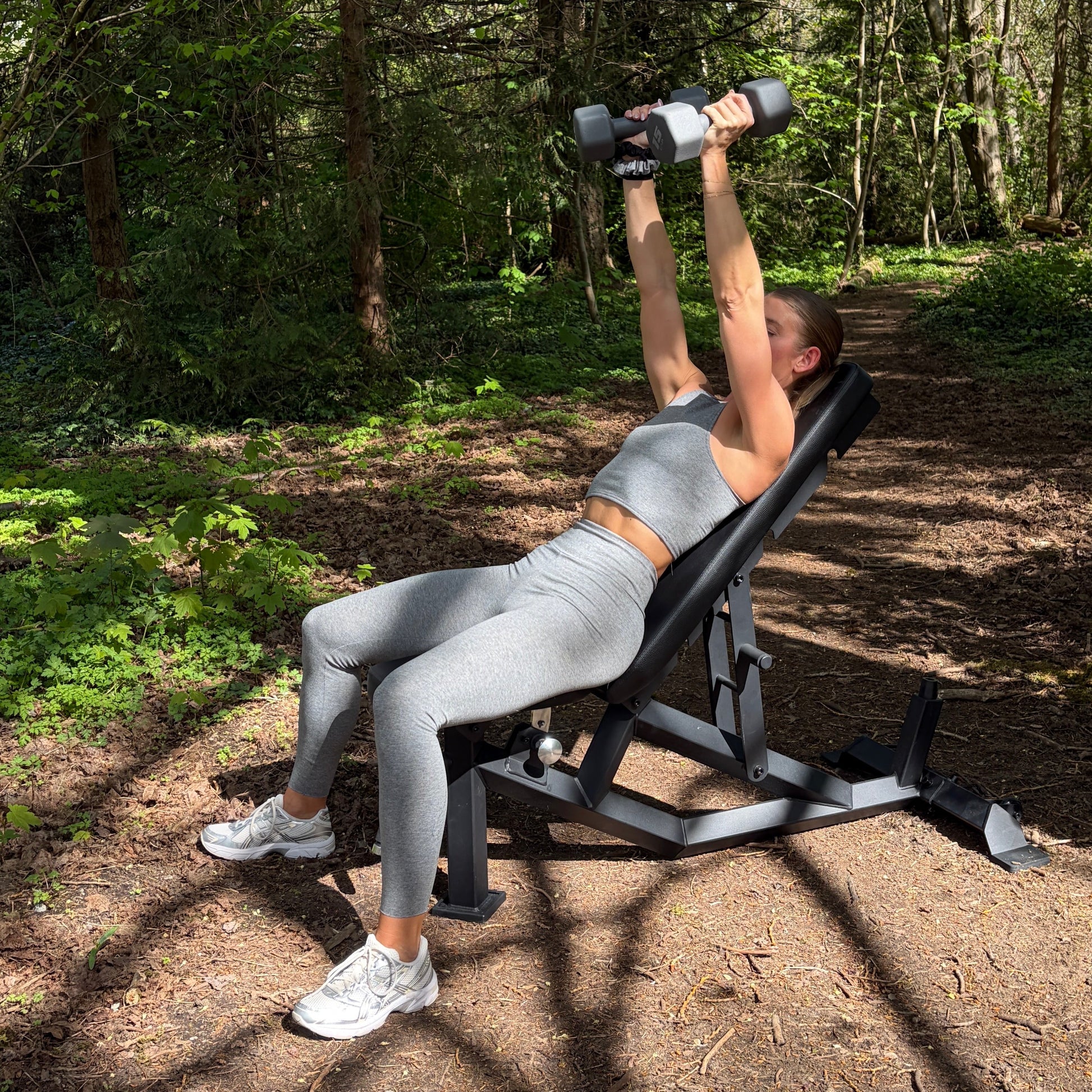 Person exercising with dumbbells on a bench in a forest setting