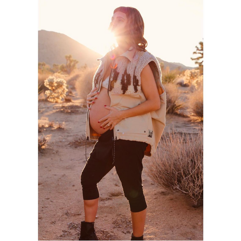 Pregnant woman standing in a desert landscape with mountains in the background