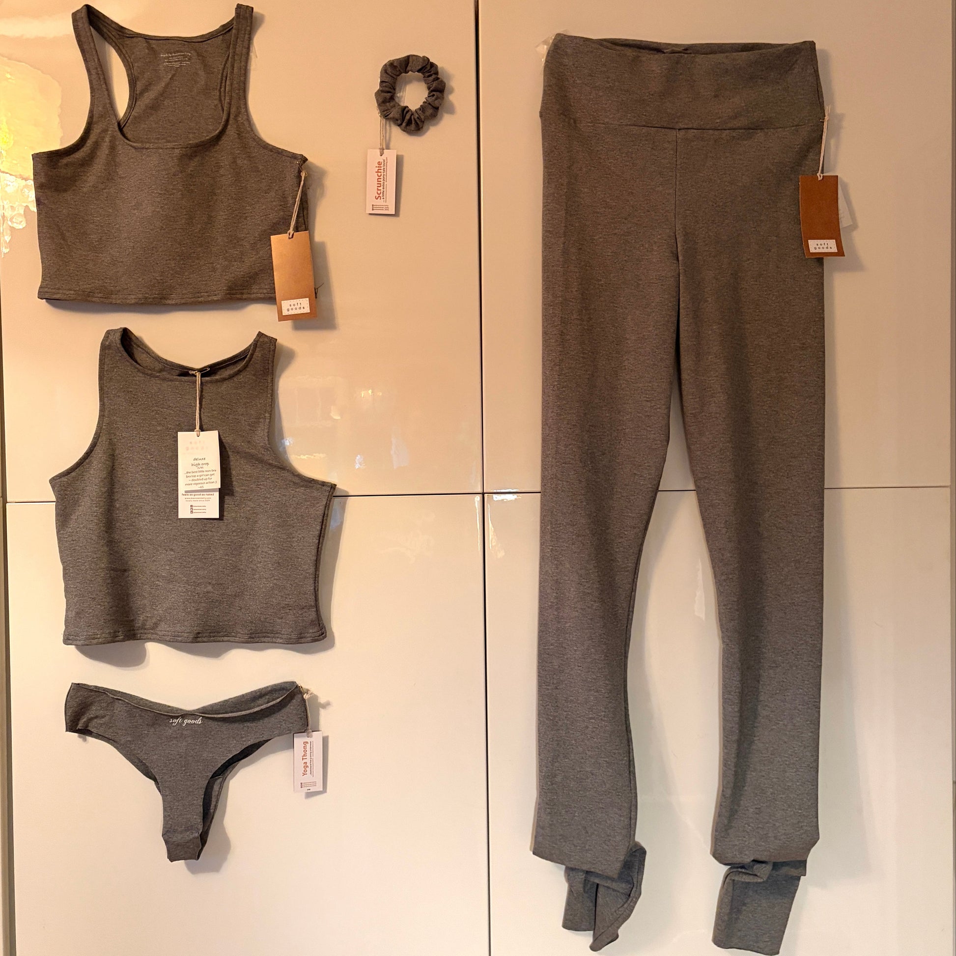 Gray athletic wear set with leggings, sports bras, and underwear on a tiled wall.