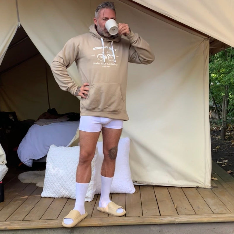 Person standing outside a large beige tent wearing a hoodie and shorts.