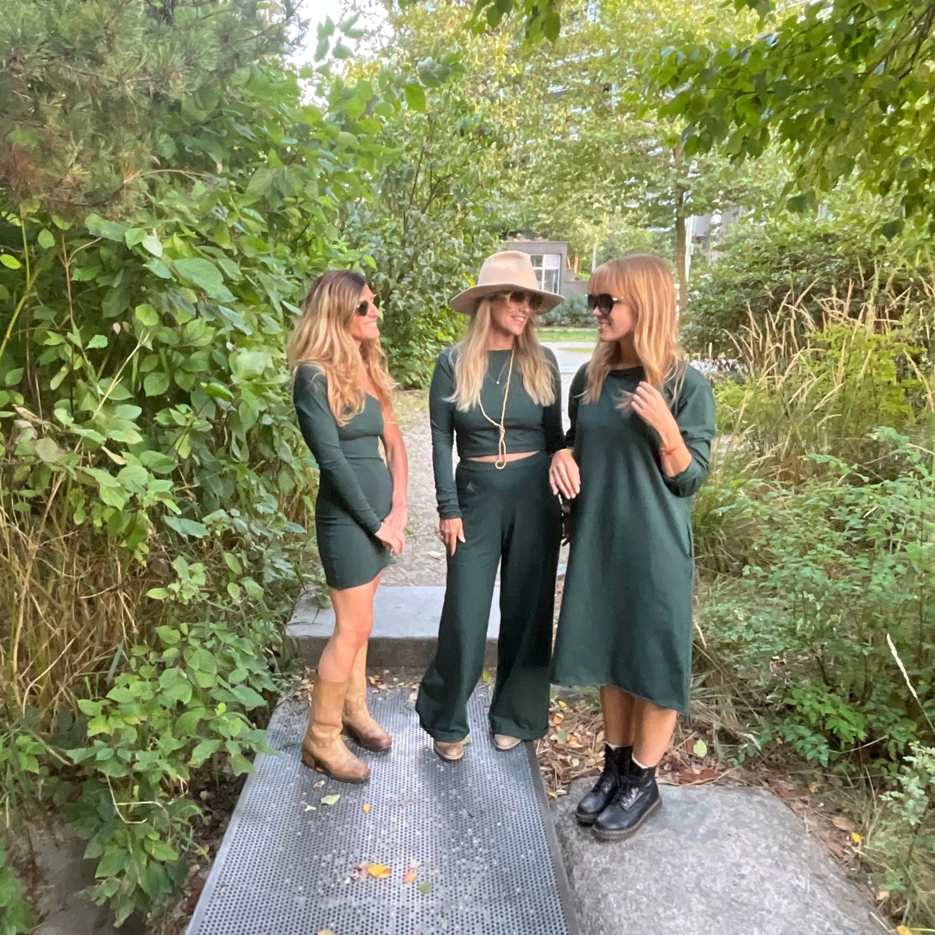 Group of people in green outfits, all standing on a path surrounded by trees.