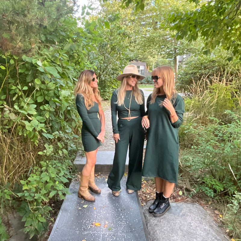 Group of people in green outfits, all standing on a path surrounded by trees.