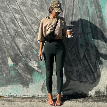 woman in front of feather/ wing mural, wearing leggings, drinking coffee