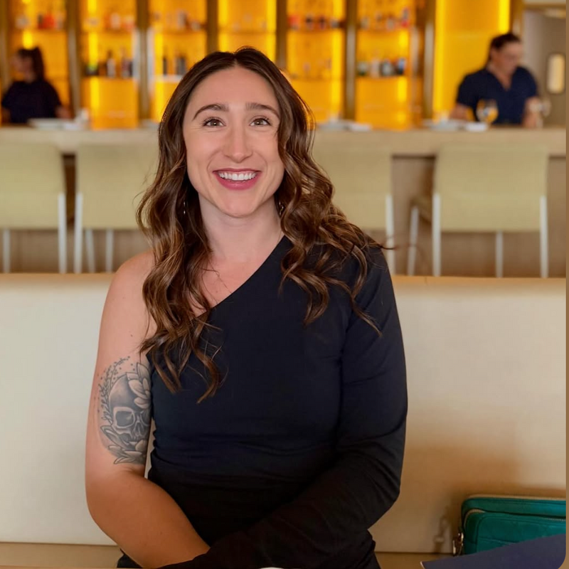 Person in a black outfit sitting
 in a restaurant setting with a blurred background