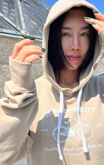 Person wearing a beige hoodie with a  dtbbicycle logo, standing outdoors.