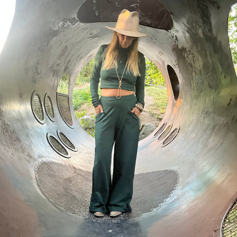 Person standing inside a large tunnel structure, wearing a hat with a green longsleeve shirt & trousers 
