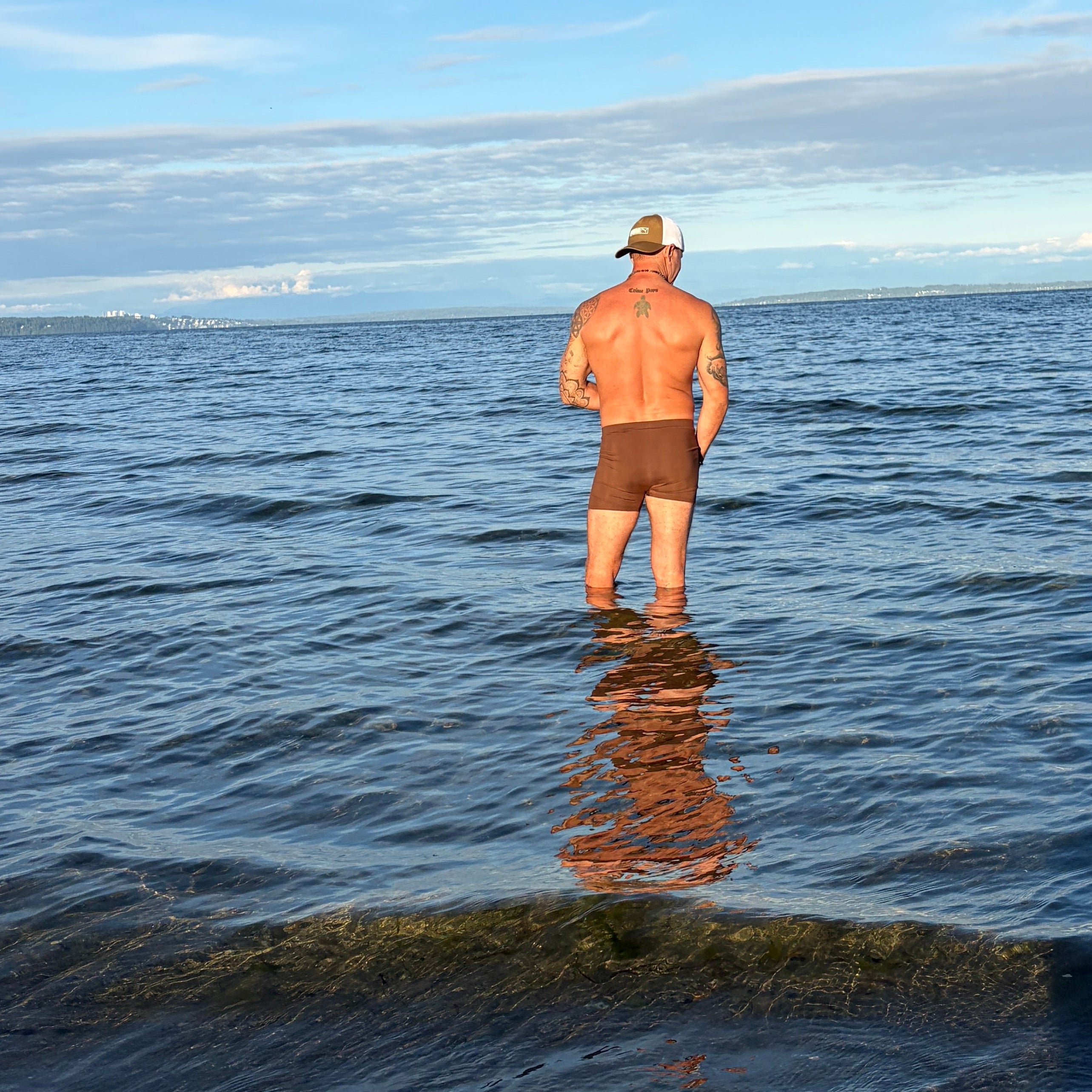 Man standing in the ocean with a clear blue sky and clouds.
