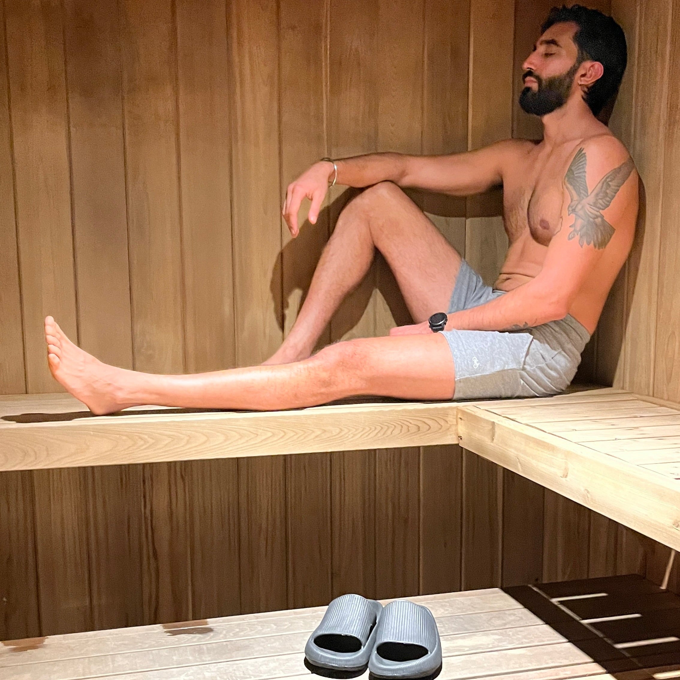 Man sitting in a wooden sauna with a pair of grey shorts on a wooden bench.