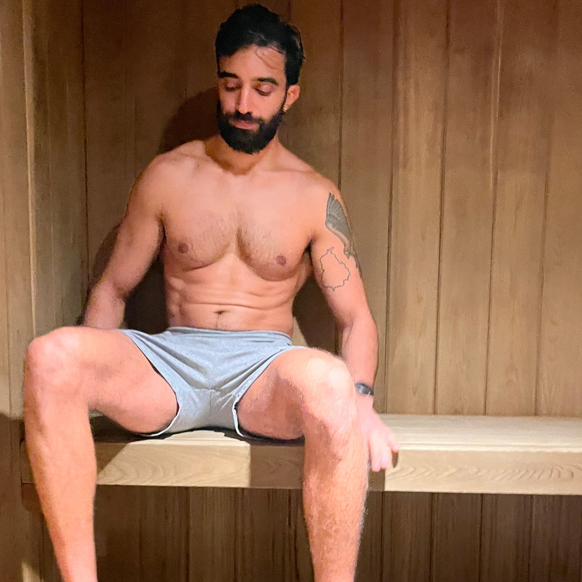 Man sitting in a wooden sauna wearing gray shorts and sandals.
