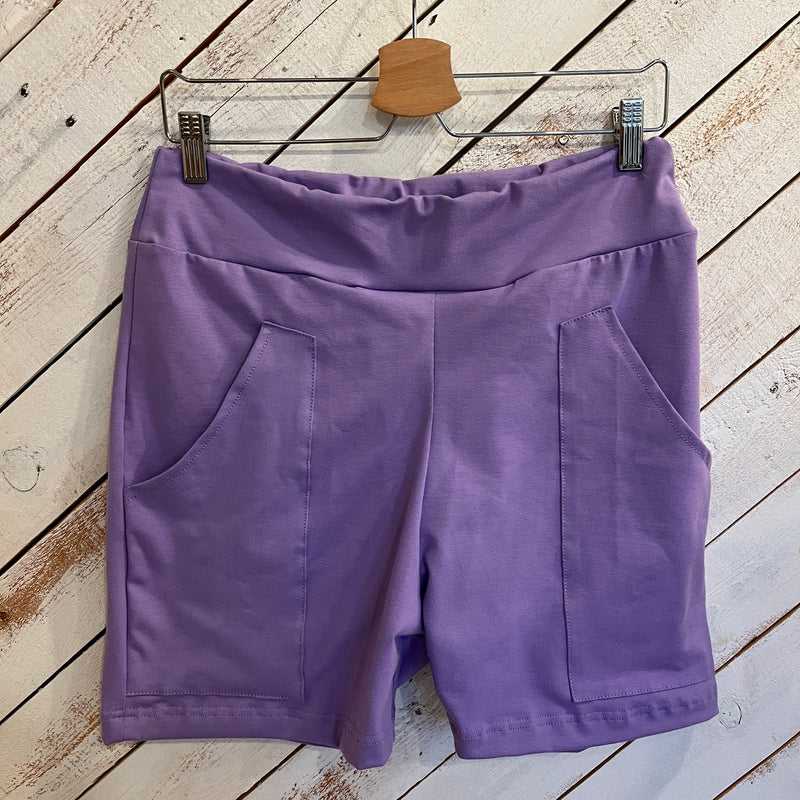 Men's mid-thigh shorts in purple hanging on a hanger on a white wooden wall