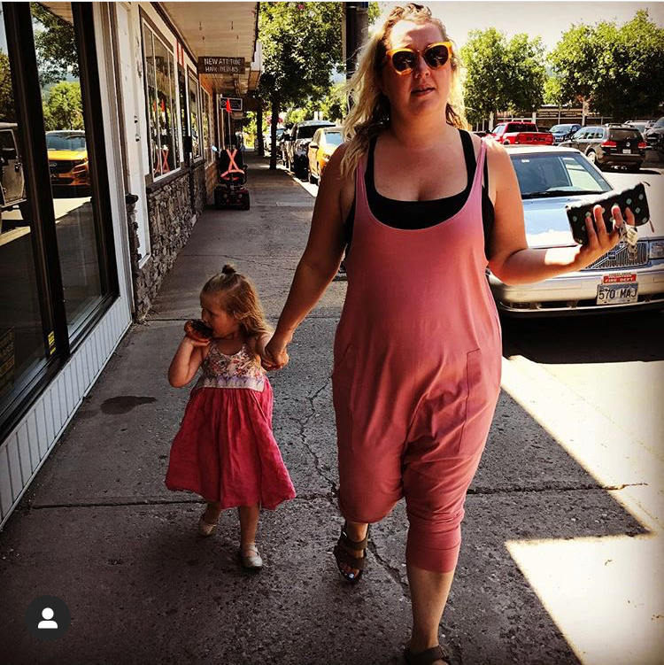 Woman and child walking on a sidewalk with a store in the background