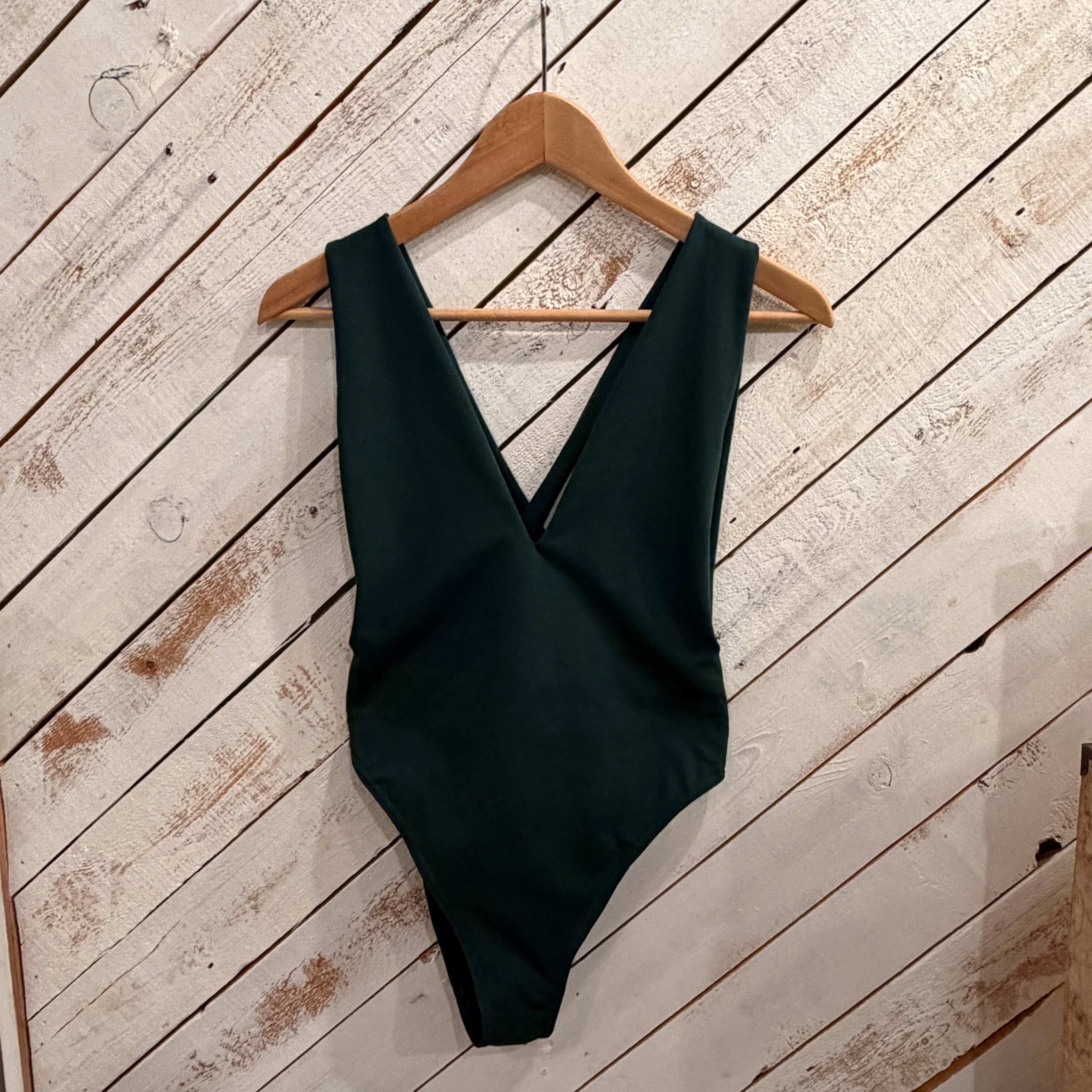 dark green swimsuit on a wooden hanger against a white wooden floor background
