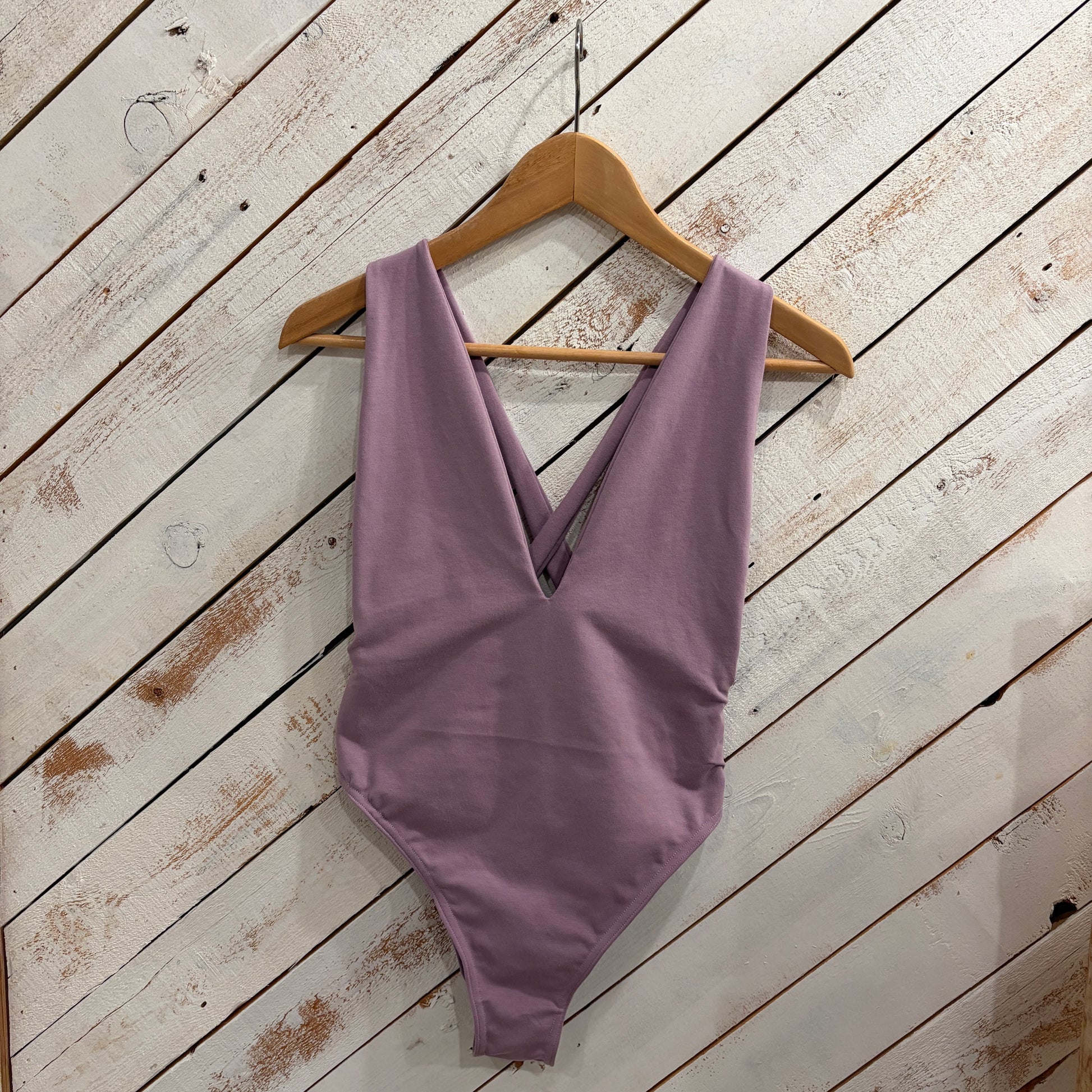 Purple swimsuit on a wooden hanger against a white wooden background