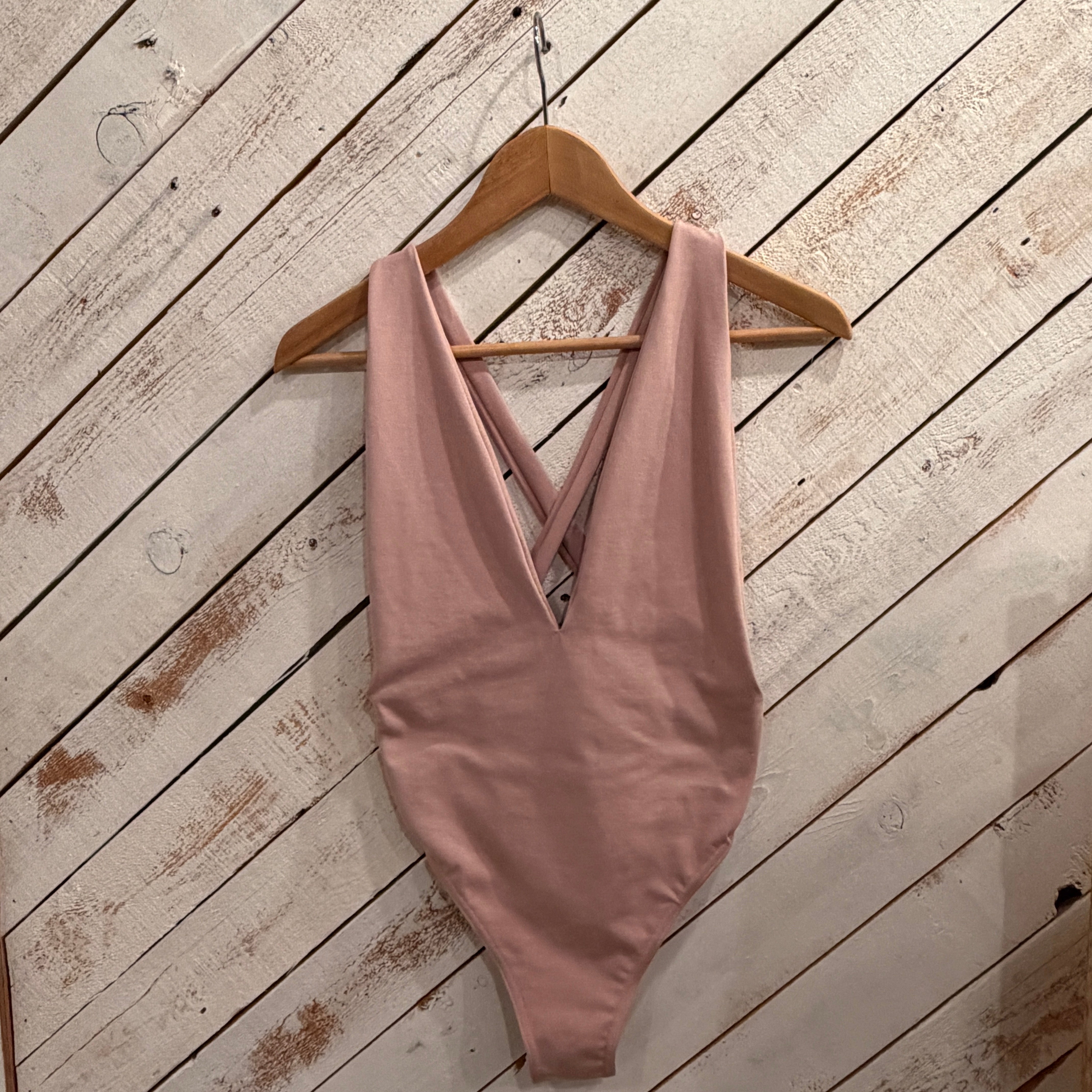 light Pink swimsuit on a wooden hanger against a white wooden barn door background