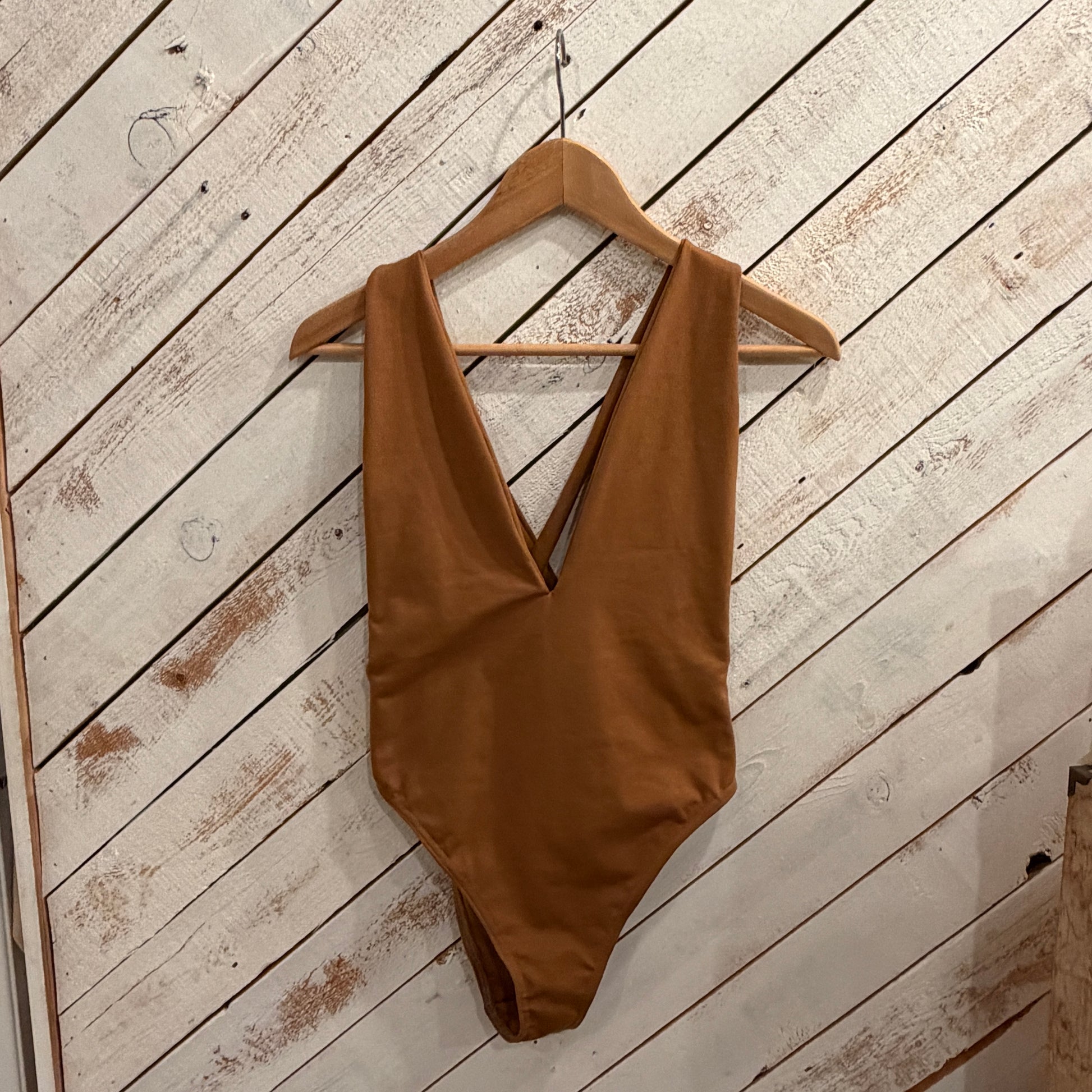 tobacco coloured swimsuit on a wooden hanger against a white wooden wall.