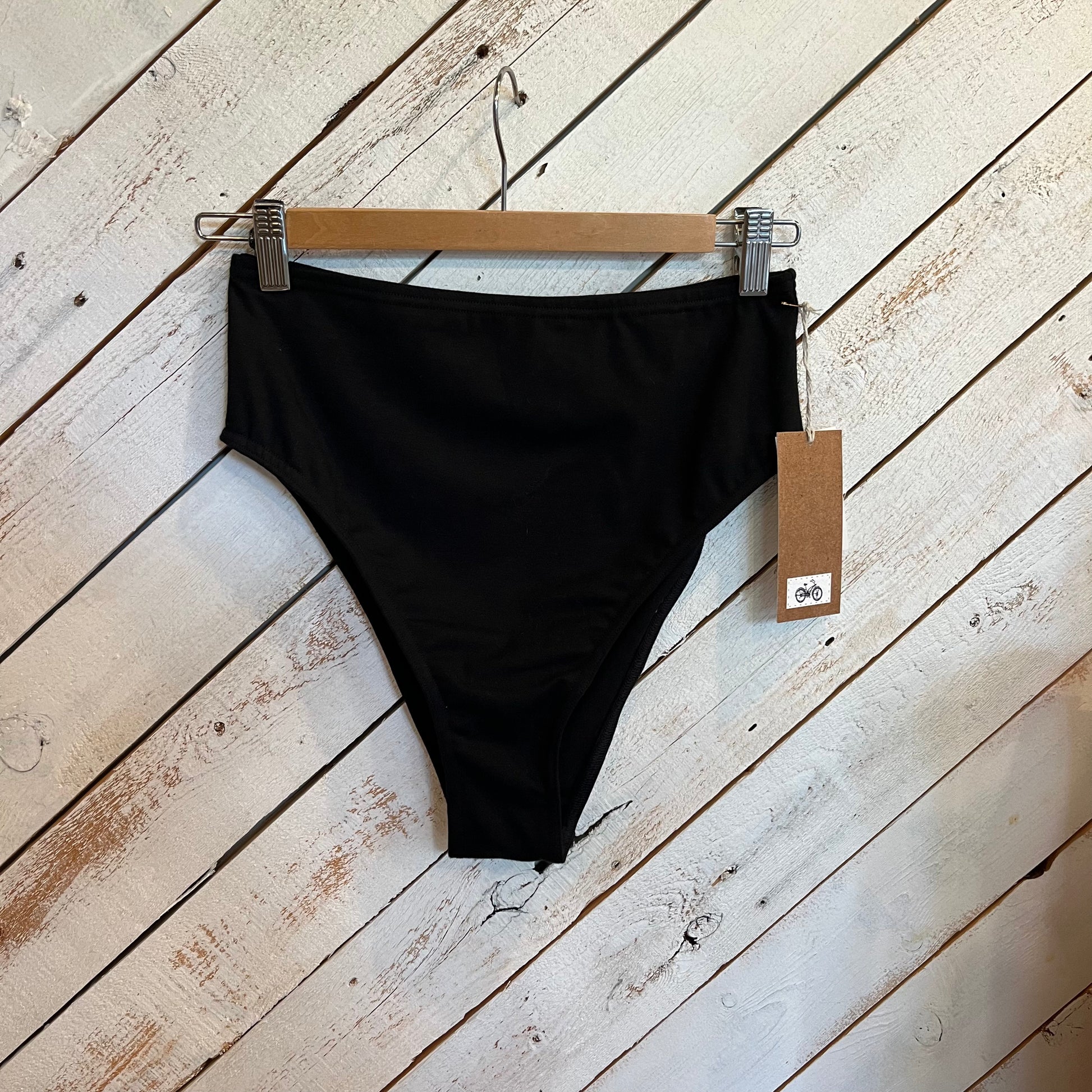 Black bikini bottom on a hanger with a tag against a wooden background