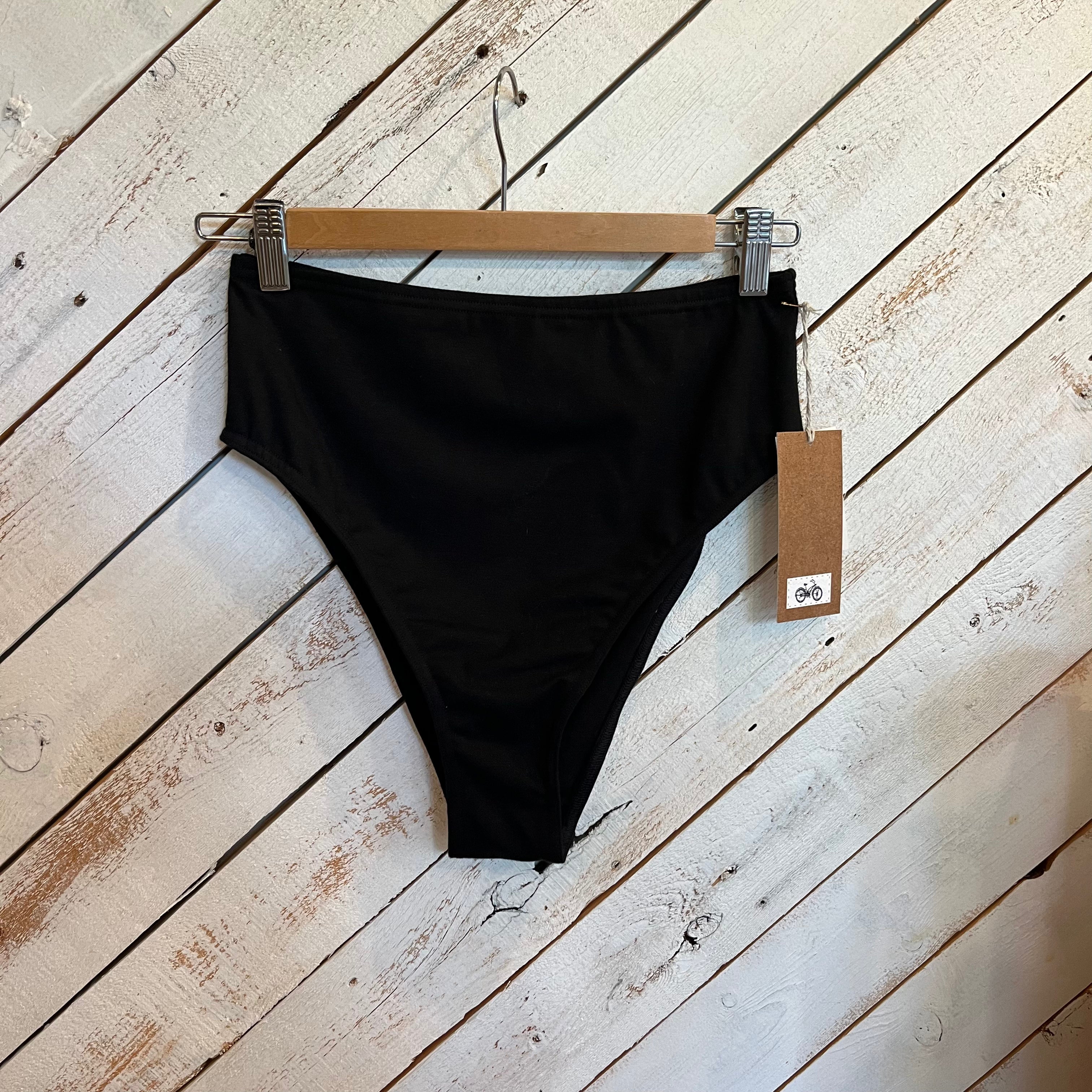 Black bikini bottom on a hanger with a tag against a wooden background