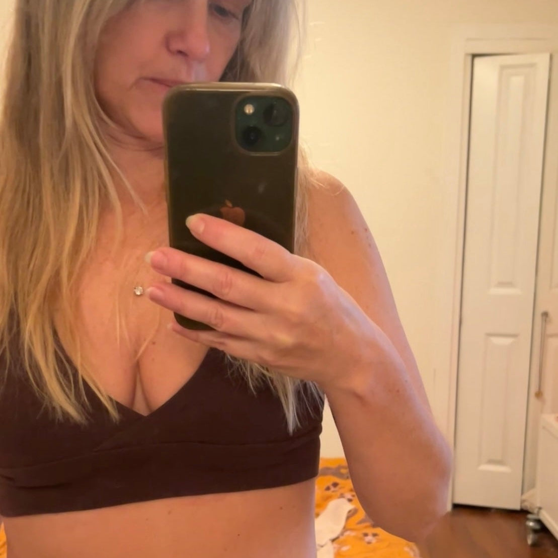 Woman taking a mirror selfie wearing a brown bikini in a room with a white door and wooden floor.