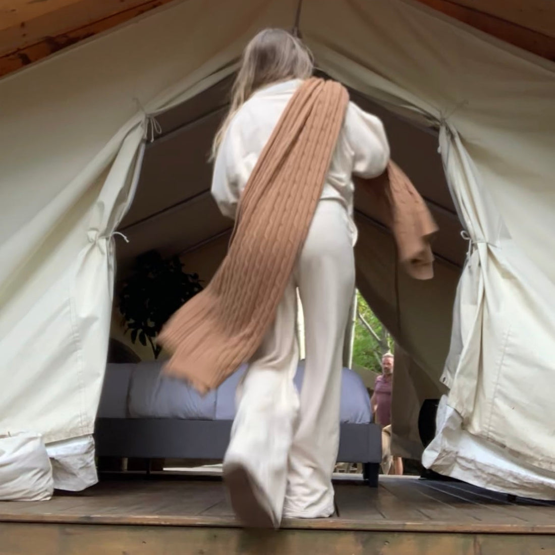 Woman in cream outfit standing in front of a glamping tent with a matching dog sitting.