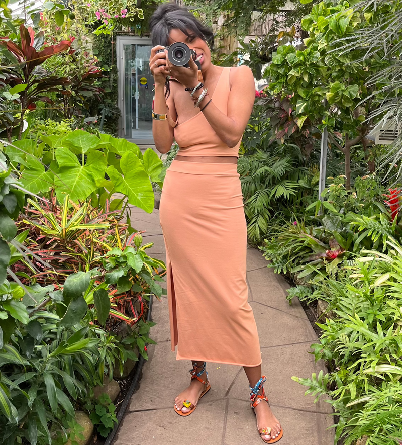 beautiful tourist with camera wearing peach natural fiber fabric skirt in plant conservatory 