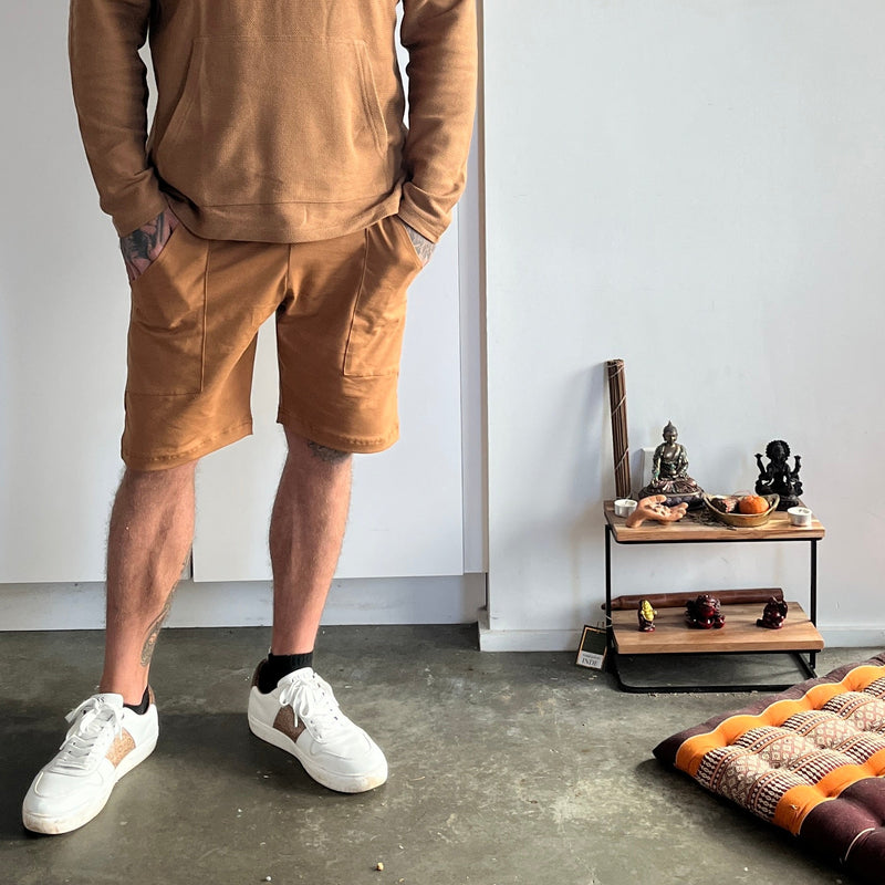 Man wearing a brown hoodie and shorts standing in a room with a small alter.