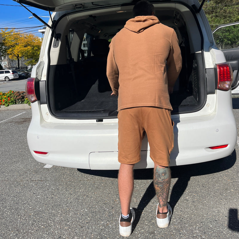 Person wearing tan pants and white shoes standing next to an open car door on a street.