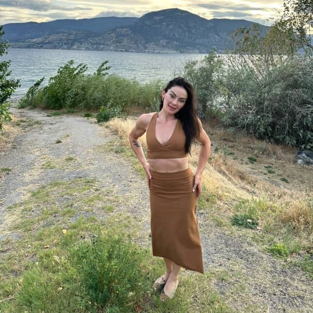 Woman standing on a path by a lake with mountains in the background