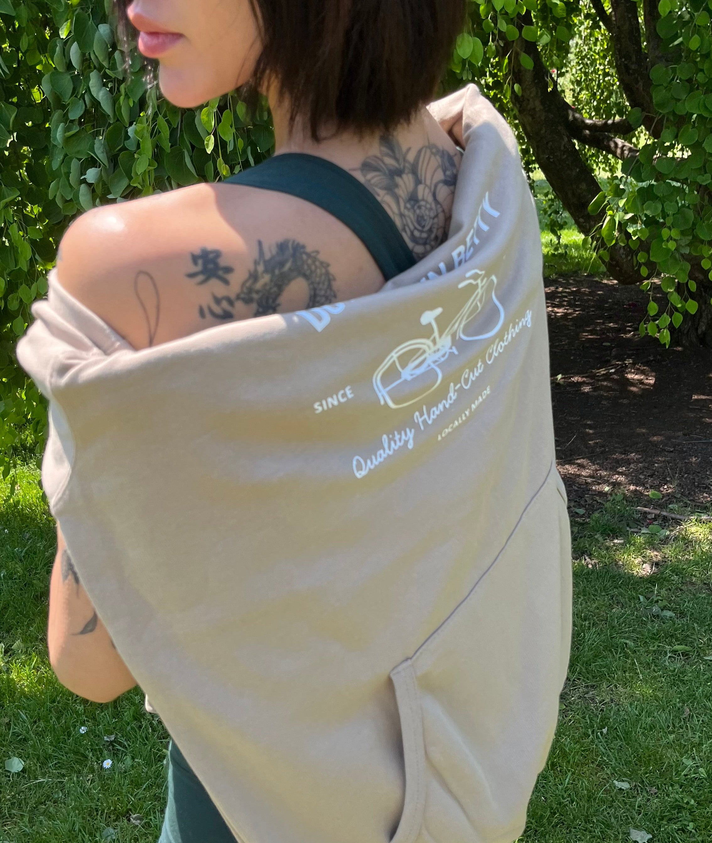 Person wearing a beige hoodie with white dtb Bicycle Loga, standing outdoors on grass.