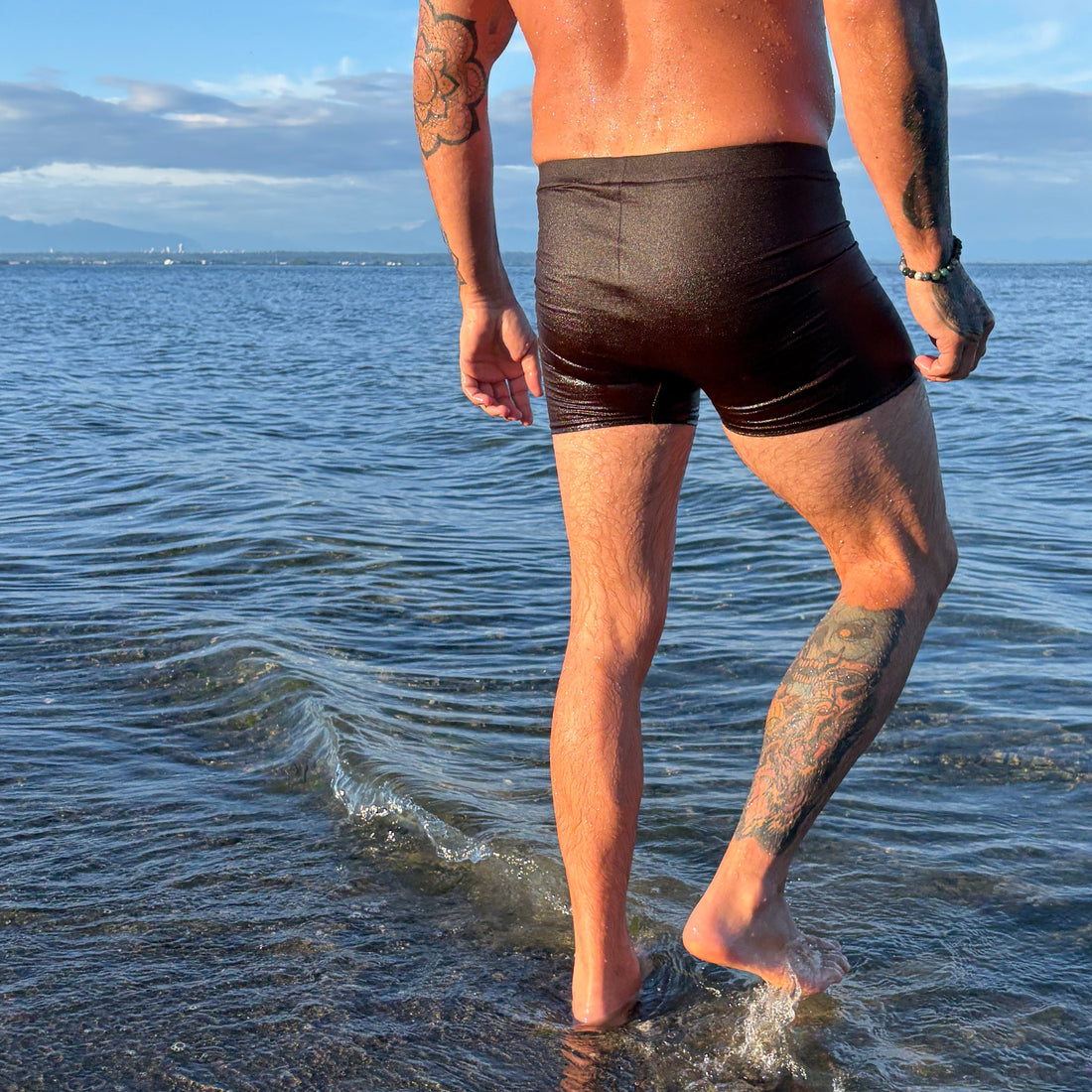 Man walking on a beach wearing dark brown swim shorts.