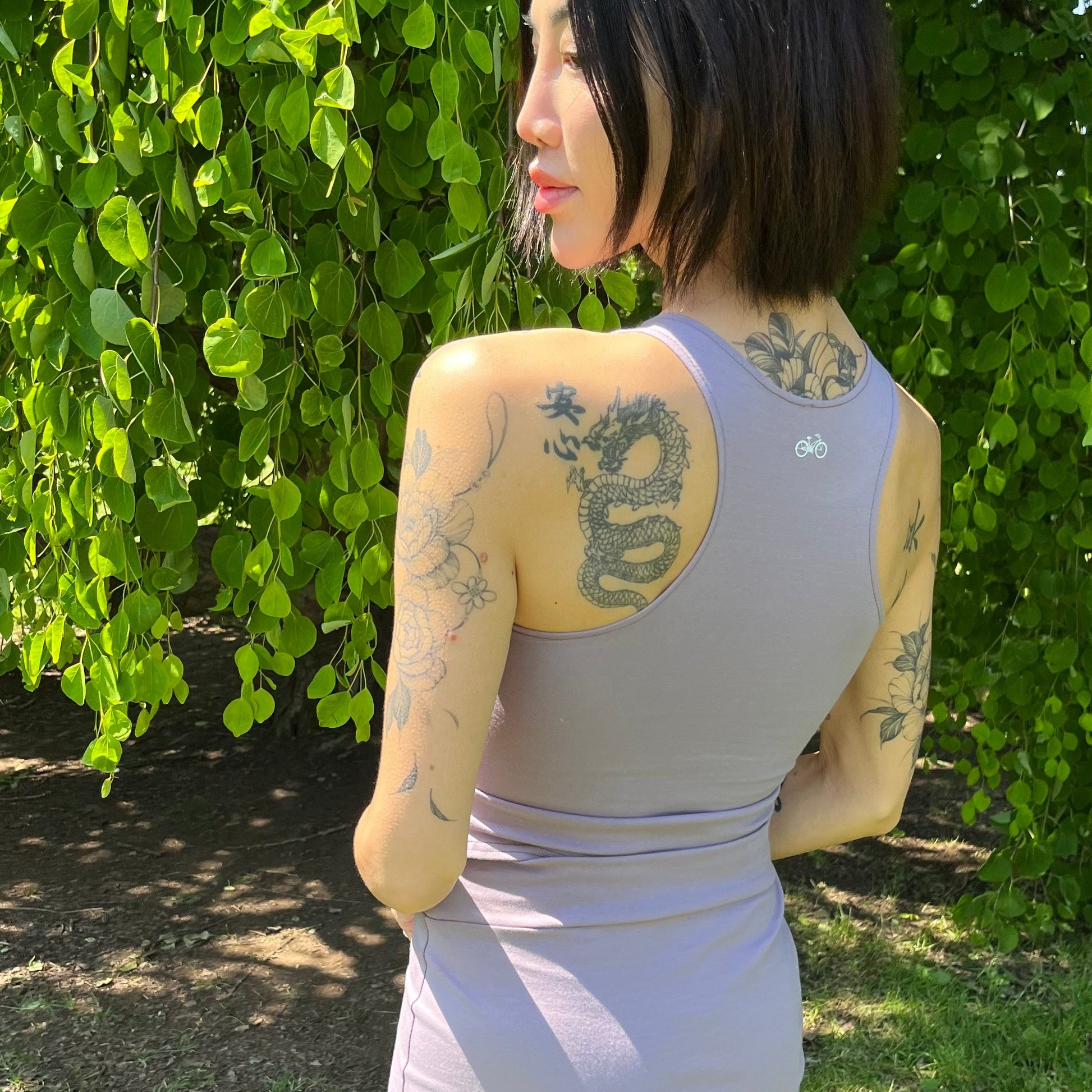 Woman in a purple outfit standing outdoors with greenery in the background