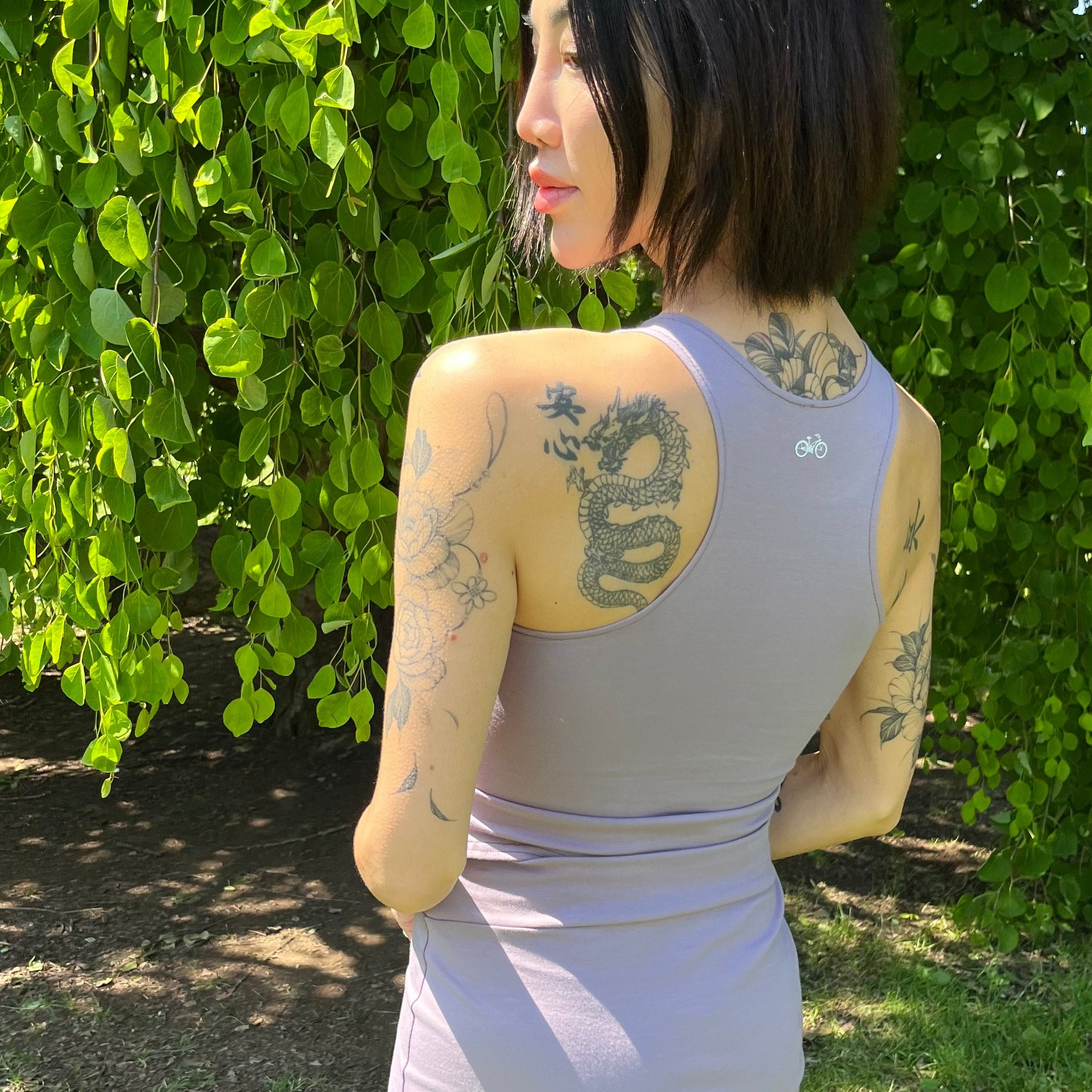 Woman in a purple outfit standing outdoors with greenery in the background