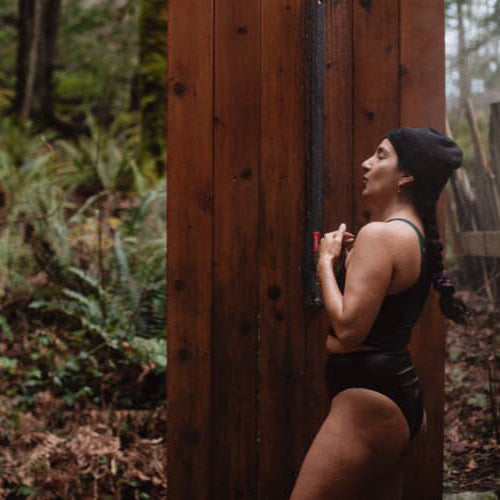 Person in natural fiber athletic wear standing against a wooden wall in a forest setting