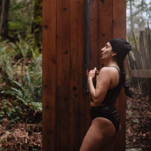 Person in natural fiber athletic wear standing against a wooden wall in a forest setting