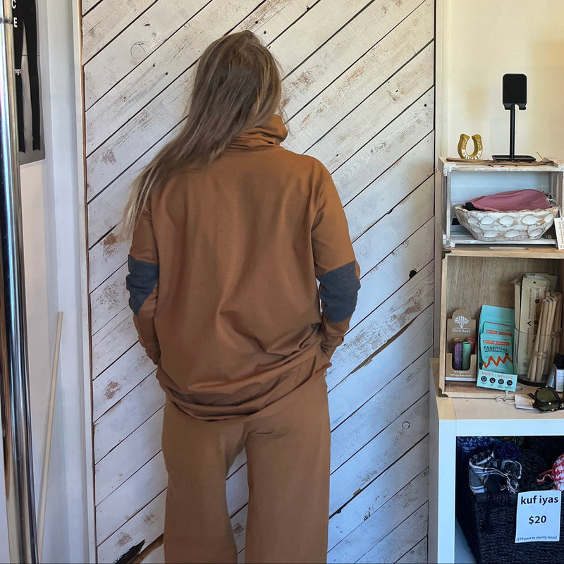 Back of Person wearing a Brown Turtleneck with elbow patches, in a room with a wooden sliding door & shelf 