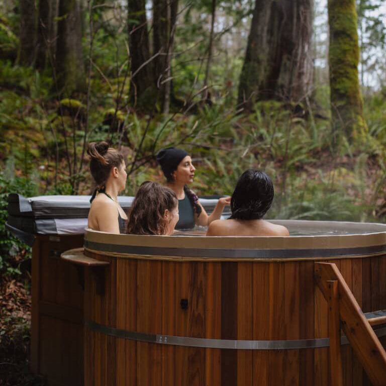 People sitting in a wooden hot tub surrounded by forest